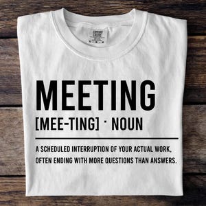 May include: White t-shirt with the word "MEETING" in large black letters. Below the word is the phonetic pronunciation and the word "NOUN". The shirt's definition of a meeting is printed below the word "NOUN".