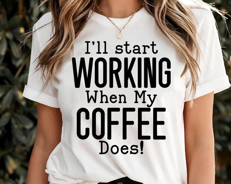 May include: White t-shirt with the text "I'll start WORKING When My COFFEE Does!" in black. The shirt has short sleeves and a round neckline. A gold necklace is visible.