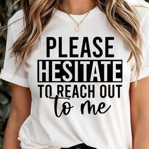 May include: White t-shirt with the text "PLEASE HESITATE TO REACH OUT to me" in black. The shirt has short sleeves and a crew neck. The text is centered on the front of the shirt.