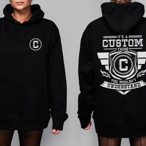 Könnte beinhalten: Schwarzer Kapuzenpullover mit einer Vordertasche und einem weißen kreisförmigen Logo mit dem Buchstaben "C". Auf der Rückseite des Hoodies steht in Weiß der Text "IT'S A CUSTOM THING YOU WOULDN'T UNDERSTAND", zusammen mit einem Schilddesign und dem Buchstaben "C".