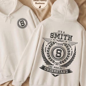 Può includere: Due felpe con cappuccio bianche. Una felpa ha un design circolare con la lettera "S" sul davanti. L'altra felpa ha il testo "IT'S A SMITH THING YOU WOULDN'T UNDERSTAND" sul retro, con una grande "S" al centro.