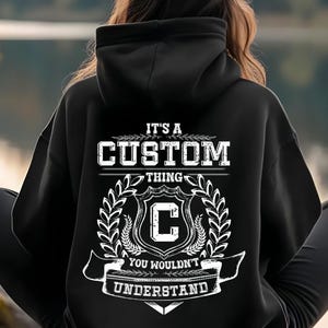 Puede incluir: Sudadera con capucha negra con un diseño gráfico blanco en la espalda. El diseño incluye las palabras "IT'S A CUSTOM THING" sobre un escudo con la letra "C" y la frase "YOU WOULDN'T UNDERSTAND".