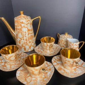 Pode incluir: Um conjunto de chá vintage com um padrão manchado creme e laranja. O conjunto inclui uma cafeteira, açucareiro, cremeira e seis xícaras e pires. Os interiores das xícaras e as alças são douradas.