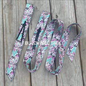 May include: A set of patterned equestrian reins with a white background, featuring pink, turquoise, and black designs. The reins have a repeating pattern of cacti, horseshoes, and other western-themed elements. The text "BURCH HILL TACK" is visible.