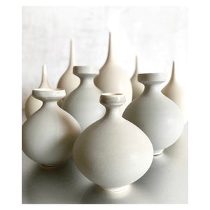 May include: A collection of white ceramic vases with varying shapes and sizes. The vases are arranged in a staggered formation, creating a visually appealing display.