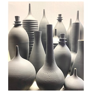 May include: A collection of gray ceramic vases of various shapes and sizes. The vases are arranged in a cluster, with some overlapping. The vases are all made of a smooth, matte ceramic.