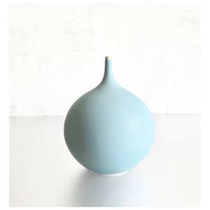 May include: A light blue ceramic vase with a rounded body and a narrow neck.