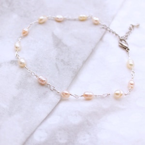 May include: A delicate bracelet featuring small, irregular, cream-colored freshwater pearls spaced along a thin, silver-toned wire chain. The piece includes a lobster claw clasp and a short extender chain with a small metal link at the end.