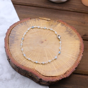 May include: A delicate bracelet featuring a thin silver-toned chain interspersed with small, round, translucent light blue beads. The jewelry piece is secured with a metal lobster claw clasp, showcasing a simple and refined design with consistent spacing.