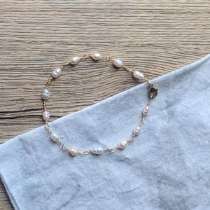 May include: A delicate bracelet featuring small, irregular white freshwater pearls spaced evenly along a thin gold-toned metal chain. The piece is secured with a small lobster claw clasp, showcasing a simple design with natural pearl shapes.