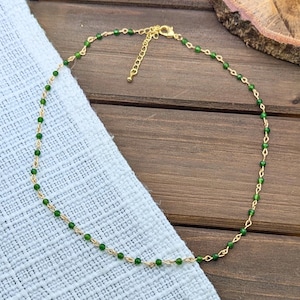May include: A delicate gold-tone chain necklace featuring small, round, vibrant green beads spaced evenly along the length. The necklace includes a gold-tone lobster claw clasp and an adjustable extender chain with several links for length variation.