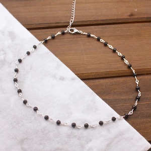 May include: A delicate silver-toned chain necklace featuring evenly spaced, small, round, faceted black beads. The necklace includes a thin silver-toned metal chain with a lobster claw clasp and an adjustable extender chain at the back.