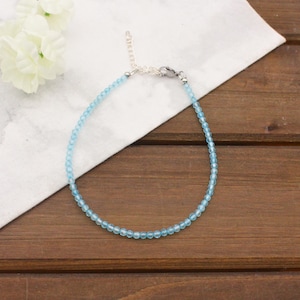 May include: A delicate anklet featuring a single strand of small, light blue beads. The jewelry piece includes a silver-toned metal chain extender and a lobster claw clasp, allowing for adjustable length to fit various sizes comfortably.