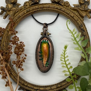 May include: A copper and wood pendant necklace featuring a green and orange iridescent beetle encased in a wooden frame with green stitching.
