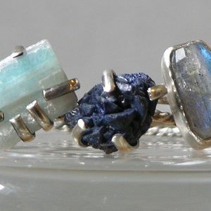 May include: Three silver rings with different gemstones. The first ring features a light blue aquamarine stone, the second ring has a dark blue stone, and the third ring has a light blue moonstone.