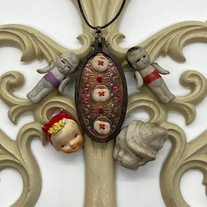 May include: A brown wooden oval frame with red embroidery and a copper finish. The frame is surrounded by five porcelain figurines, including a devil, a cherub, and three children.