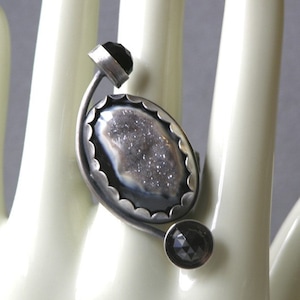 May include: A silver ring with a white and black agate stone set in a silver bezel. The ring has a black stone accent on the side.