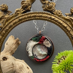 May include: A copper pendant necklace with a round, clear resin charm. The charm features a vintage map with a red, white, and green embroidered design around the edge. The map shows a creek and the word "Boulder".