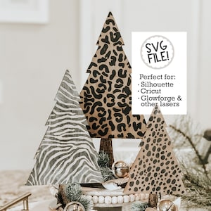 May include: Three wooden Christmas tree ornaments with different animal print designs. The trees are decorated with bells and greenery. The text "SVG FILE!" and "Perfect for: Silhouette, Cricut, Glowforge & other lasers" is visible in the image.