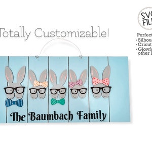 May include: A blue wooden sign with the text "The Baumbach Family" and five gray bunny silhouettes with glasses and bows. The bunnies are arranged in a row and have different colored bows.