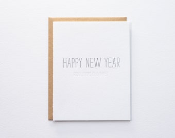 May include: A white card with a brown envelope. The card has the text "Happy New Year" and "Resolutions be damned" in black.