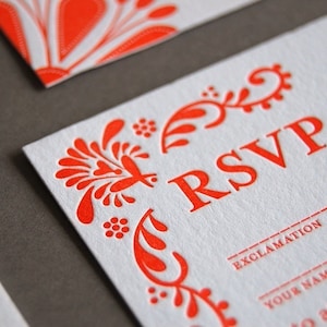 May include: A white RSVP card with a red floral design and the word "RSVP" in large red letters. The text "Please fill in" is also in red letters. The card has lines for the guest to fill in their name and whether they will attend.