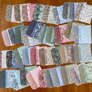 Könnte beinhalten: Eine Sammlung verschiedener floral gemusterter Papierephemera in verschiedenen Farben, darunter Rosa, Blau, Grün und Lila. Die Papierstücke sind auf einer Holzoberfläche angeordnet.