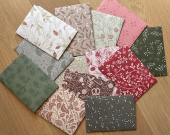 Könnte beinhalten: Eine Sammlung rechteckiger Papierumschläge mit verschiedenen weihnachtlichen Mustern, darunter Tannenzapfen, Stechpalmenblätter, Beeren, Glocken, Brezeln und Schneeflocken in den Farben Rot, Grün, Weiß, Rosa, Braun und Dunkelgrau.