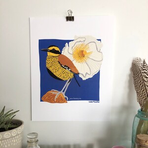 May include: A print of a yellow and black bird with a brown breast perched on a rock with a white flower behind it. The background is blue. The print is signed "kate burke".