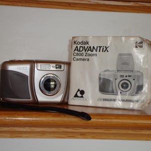 May include: A silver and gray Kodak Advantix C800 Zoom camera with a black strap sits next to its packaging. The packaging features a picture of the camera and the text "Kodak ADVANTIX C800 Zoom Camera".