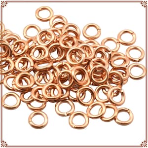 May include: A collection of copper-colored jump rings, scattered across a white surface. The rings are circular, with a split for attaching to other components. Ideal for jewelry making and crafting projects.