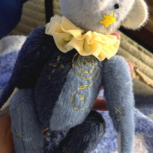 Può includere: Un orsacchiotto fatto a mano in tonalità blu, con una stella e un colletto gialli. L'orso presenta dettagli di cuciture dorate. Un giocattolo artigianale e affascinante.