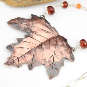 May include: A copper leaf pendant necklace with a hammered texture and detailed veins. The necklace features a silver chain and carnelian beads.