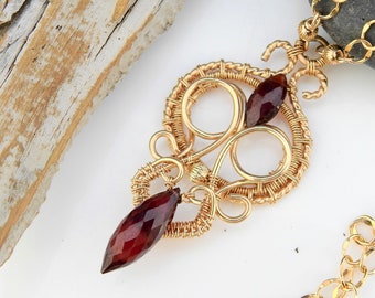 May include: A gold wire wrapped pendant with two dark red gemstones. The pendant is attached to a gold chain.