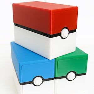 以下が含まれることがあります： ポケモンのモンスターボールを模した3つの積み重ねられた収納ボックス。一番上のボックスは赤、真ん中は白、下のボックスは青と緑です。各ボックスには黒いストライプと白い円があります。