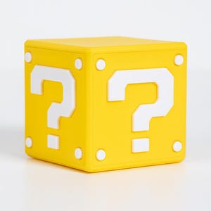 Könnte beinhalten: Ein gelber Würfel mit weißen Fragezeichen auf jeder Seite. Weiße kreisförmige Details befinden sich an den Ecken. Das Design ist von einem beliebten Videospiel inspiriert.