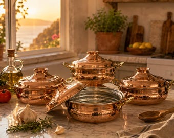 May include: A set of four hammered copper pots with matching lids and gold-toned handles. The pots feature a polished metallic finish and rounded bodies. One lid is placed beside a pot, revealing a silver-toned interior lining.