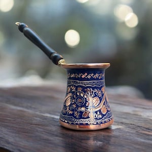 May include: A traditional Turkish coffee pot with a blue and gold floral design. The pot has a wooden handle and a copper base.