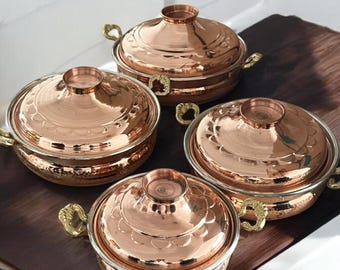 May include: Set of four copper serving dishes with lids and gold handles. The dishes have a hammered finish and a decorative design.
