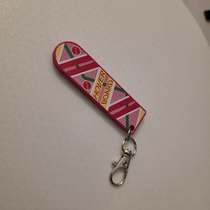 May include: A red and pink hoverboard keychain with the words "HOVER BOARD" in yellow. The keychain has a silver clasp and ring. The hoverboard design features diagonal stripes and circular accents.