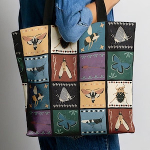 May include: A black tote bag with a colourful patchwork design featuring various insects and butterflies. The bag has black handles and a white background with a repeating pattern of squares.