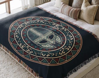 May include: A dark navy blue woven throw blanket featuring a large central circular design. The graphic depicts a detailed helmet with intricate knotwork patterns, surrounded by a geometric border of triangles in teal, red, and cream colors.