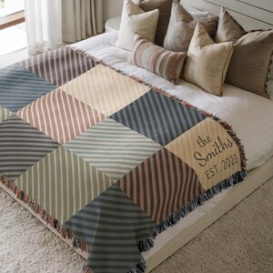 May include: A patterned throw blanket in shades of blue, green, and beige, with a geometric design of squares and striped patterns. The blanket has a fringed edge and the text "the Smiths EST. 2023" is displayed.