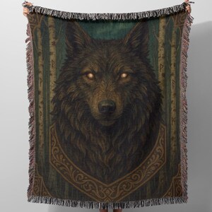 Peut inclure: Une couverture tissée avec une illustration détaillée d'une tête de loup aux yeux jaunes brillants. Le loup est brun avec une texture de fourrure détaillée, sur fond de rayures verticales vertes et marron et de bordures décoratives. La couverture a une bordure frangée.