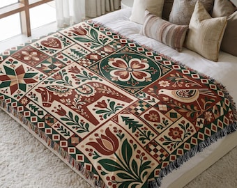 May include: A woven throw blanket featuring a repeating grid pattern of folk-inspired motifs including a Dala horse, stylised tulips, birds, hearts, and geometric stars in a colour palette of deep red, forest green, cream, and dark brown.