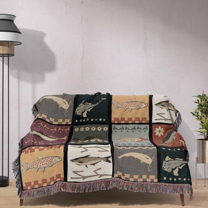 Może przedstawiać: Wielokolorowy koc z patchworkowym wzorem przedstawiającym różne ilustracje ryb. Koc ma frędzlową krawędź i jest położony na kanapie.