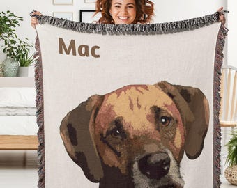 May include: A beige throw blanket with a detailed portrait of a dog with brown and tan fur. The name "Mac" is printed in brown letters at the top. The blanket has a fringed edge and is held up by a person.