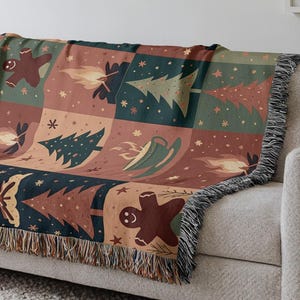 Könnte beinhalten: Eine gewebte Decke mit einem Patchwork-Design mit Lebkuchenmännern, Weihnachtsbäumen und anderen Illustrationen zum Thema Feiertage in Braun-, Grün- und Rottönen. Die Decke hat einen Fransenrand und ist über ein Sofa drapiert.