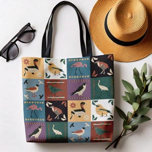 May include: A black tote bag with a colourful pattern of birds and geometric shapes. The bag has a black handle and is made of canvas.
