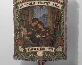 May include: A woven throw blanket featuring a library scene with two people reading books and a cat. The text reads MY FAVORITE CHAPTER IS YOU, THEO & IMOGEN, and 2026. The design includes floral borders, bookshelves, and a window.